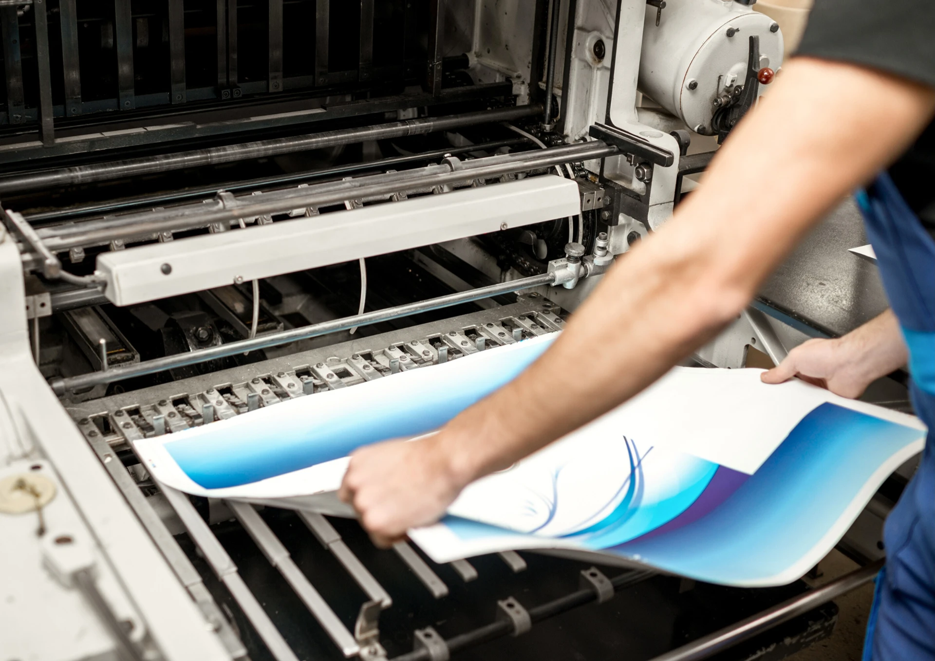 Imagen de un maquinista de imprenta revisando varios pliegos de papel recién imprimidos